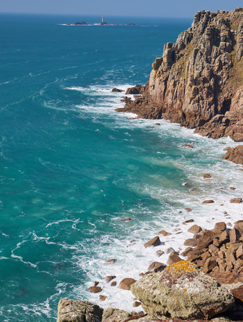 Longships lightouse cliffs This landscape photograph captures the rugged cliffs of Cornwall’s coast in the United Kingdom during the early afternoon of spring. The main subject is the Longships Lighthouse cliffs, with steep rock faces descending to the turquoise waters of the Atlantic Ocean. The presence of scattered rocks at the base of the cliffs, waves breaking along the shore, and patches of lichen and vegetation demonstrate the natural environment. In the distance, the Longships Lighthouse is visible on a rocky outcrop, serving as a landmark that helps identify the precise location along the Cornish coast. The image illustrates the powerful interplay between nature and the dramatic geology of the cliffs, highlighting the coastal scenery characteristic of Cornwall.